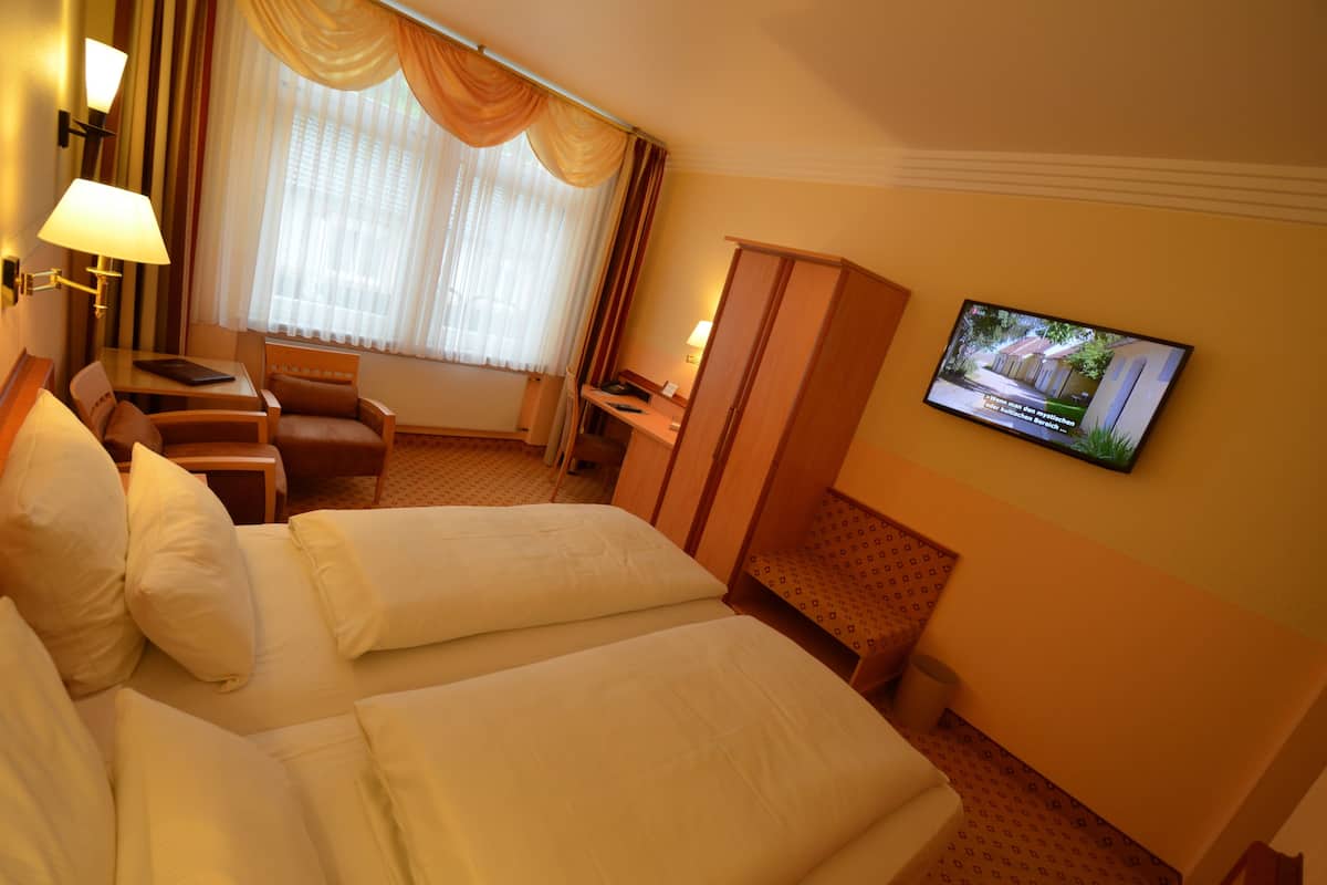 A hotel room with a bed, a desk, a chair, a television, and a window with curtains.
