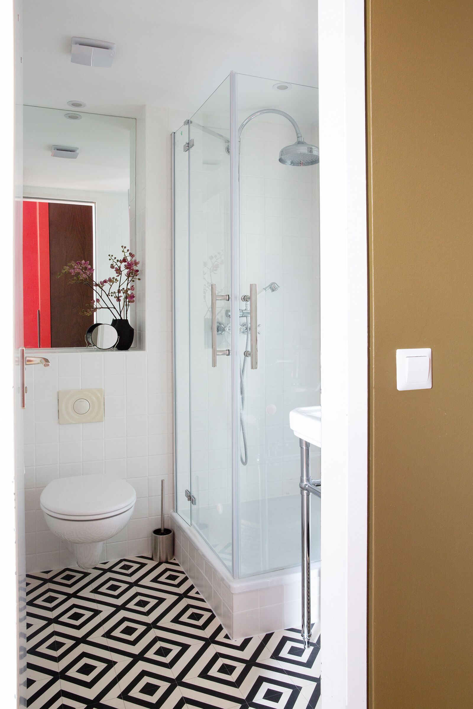 Un baño con cabina de ducha de vidrio, un lavabo blanco y un suelo estampado.