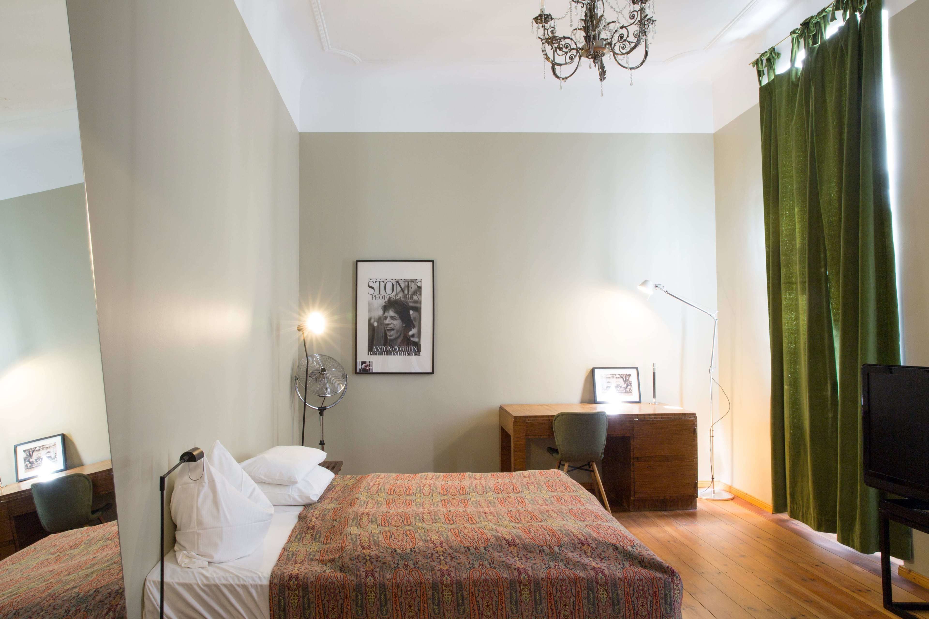 Habitación de hotel con dos camas, un escritorio, una silla, un televisor, una araña y un cuadro en la pared.