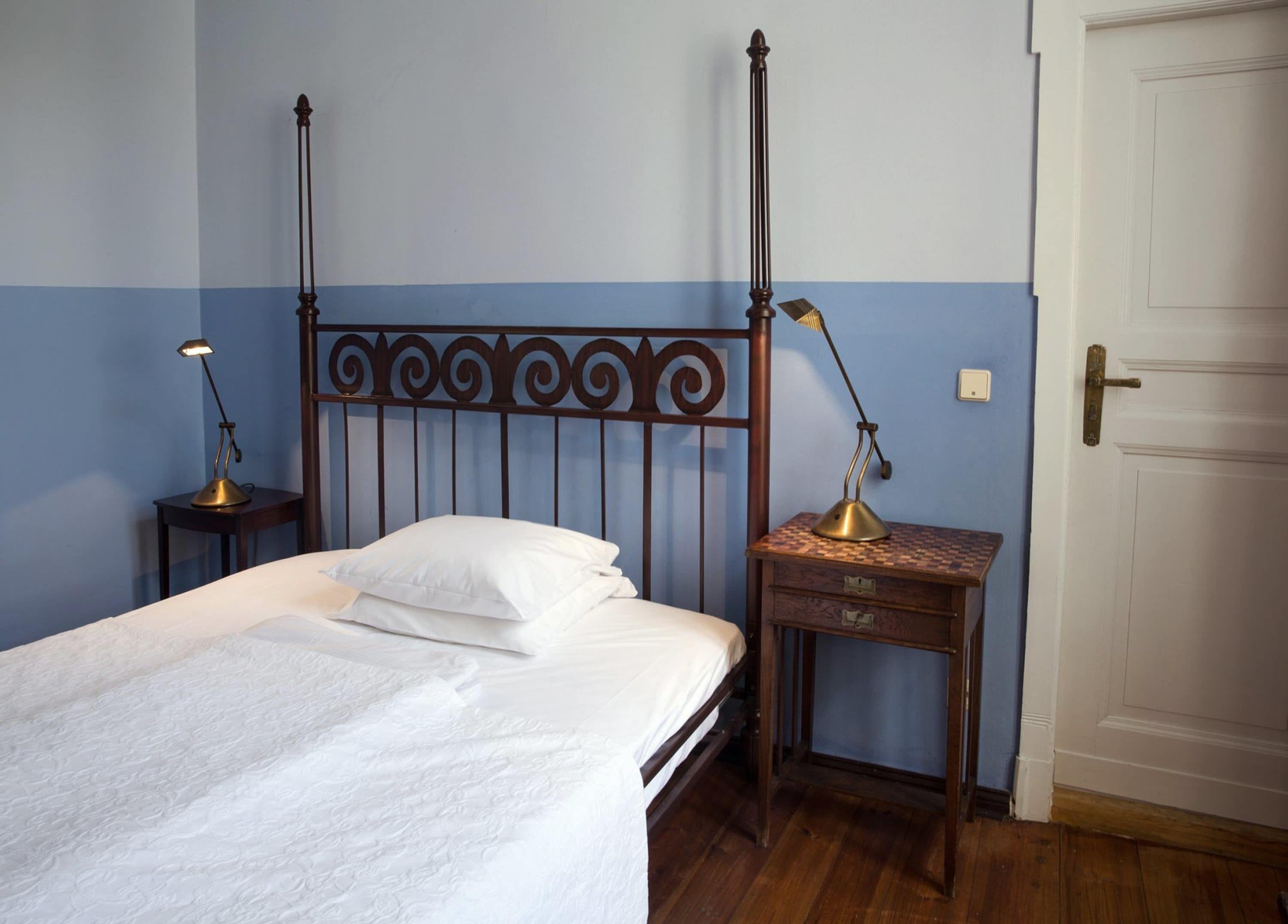Quarto com cama, duas mesas de cabeceira e uma porta.