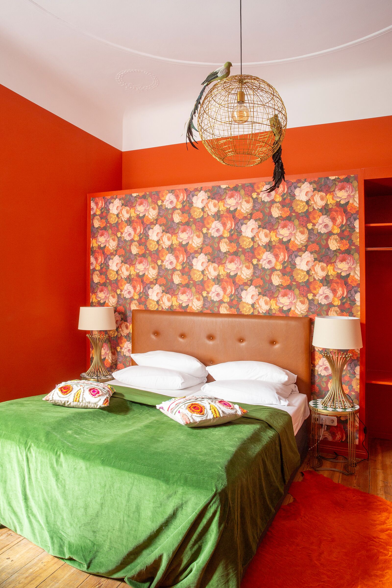 Un dormitorio con papel tapiz floral, una colcha verde y un cabecero de madera.