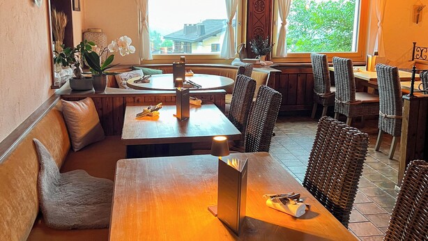 A cozy restaurant with wooden furniture, a large window with a view, and a ceiling fan. - Madrisa Lodge (Klosters-Serneus)