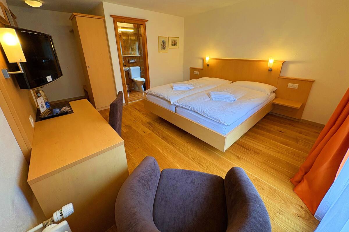 A hotel room with a bed, a desk, a chair, a television, and a bathroom visible through an open door.