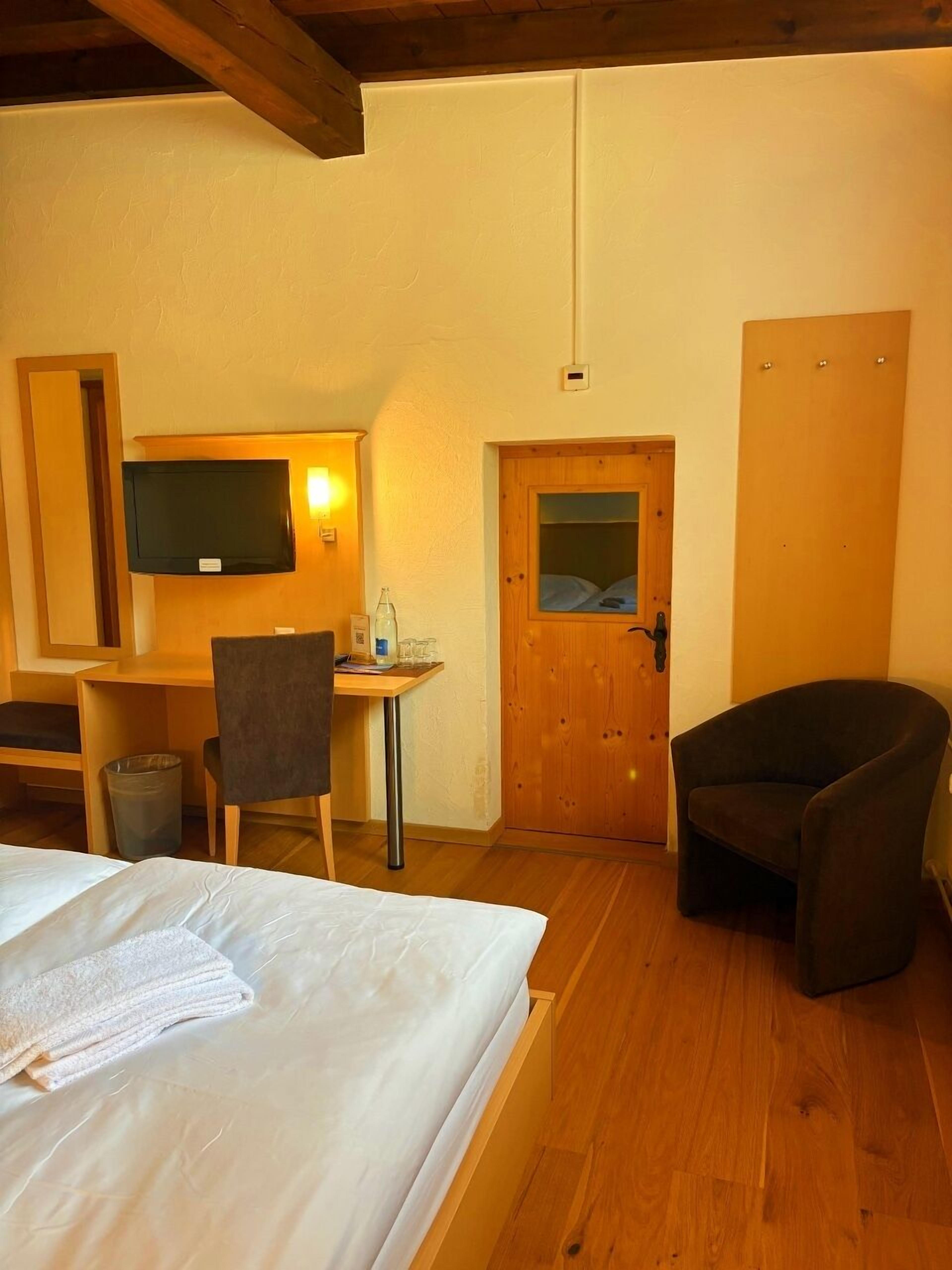 Une chambre d’hôtel avec un lit, un bureau et une chaise, une télévision et une porte en bois.