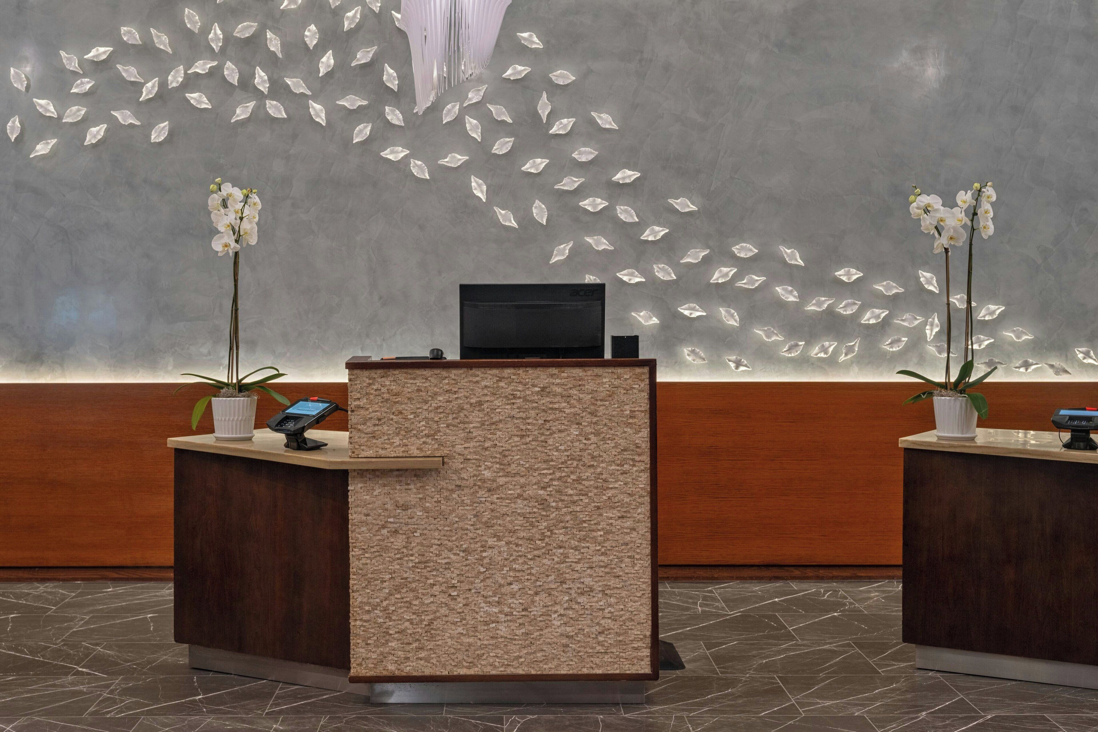 A reception desk with a textured panel, two potted orchids, and a flat-screen TV.