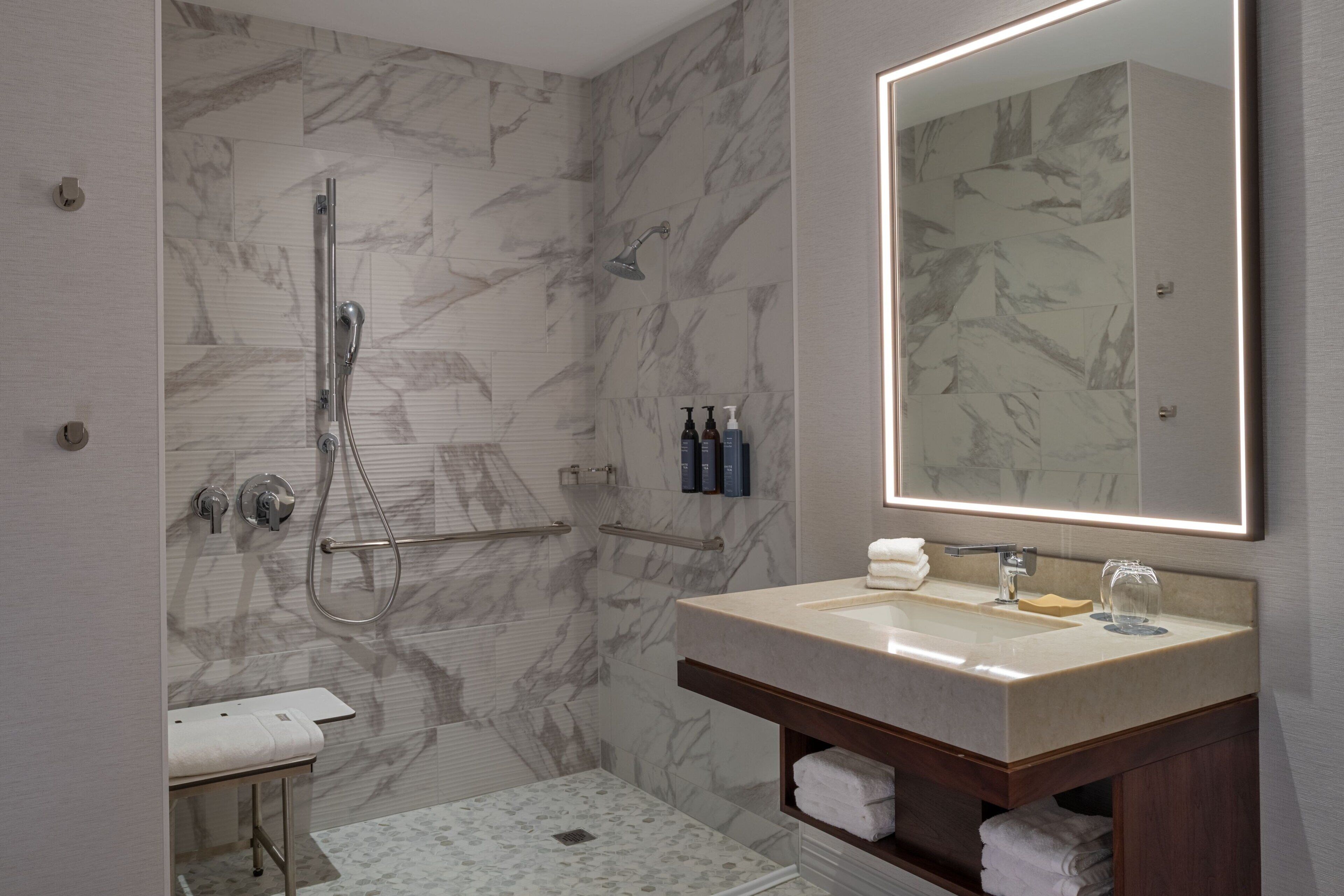 Un baño moderno con pared de ducha de mármol, un espejo grande, un lavabo con tocador y un box de ducha de vidrio.
