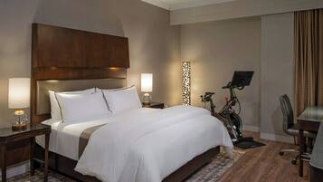 Quarto de hotel com uma cama grande, duas mesas de cabeceira com abajures, uma escrivaninha com cadeira e um ventilador de teto.