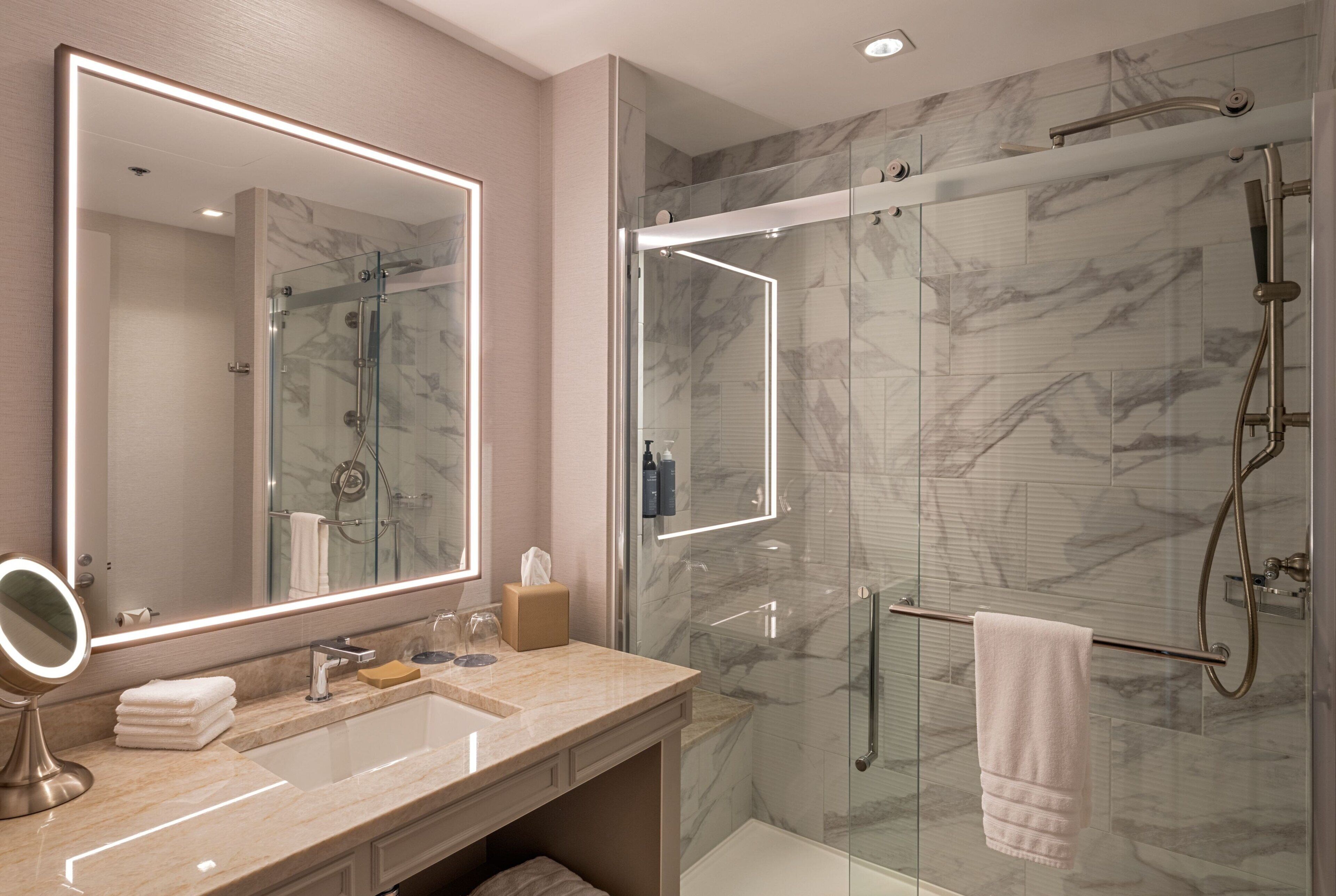 Un baño moderno con un espejo grande, un lavabo y una zona de ducha con mampara de vidrio.