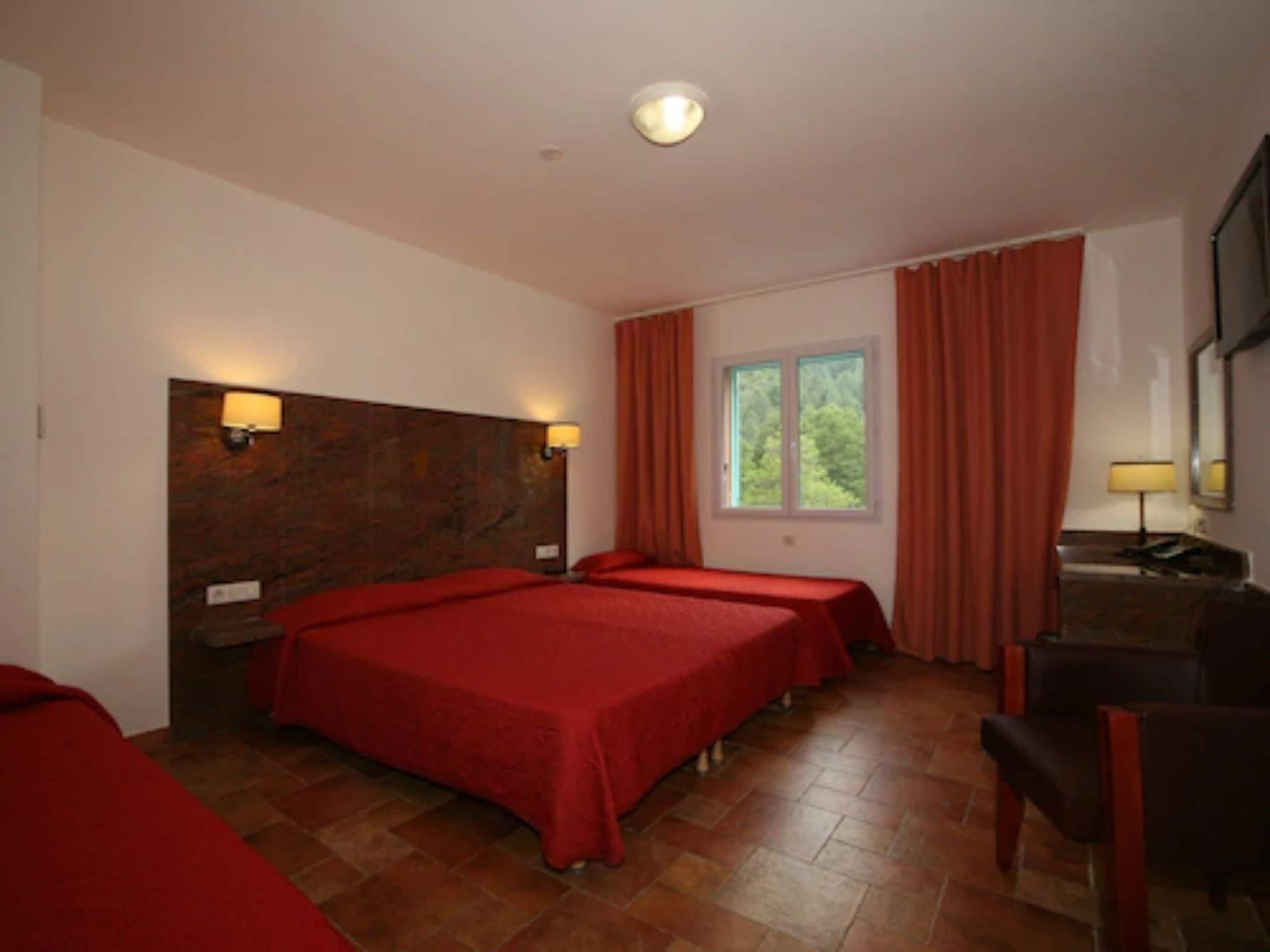 Een hotelkamer met twee bedden, een bureau, een stoel, een raam met gordijnen en een hoofdbord met wandlampen.
