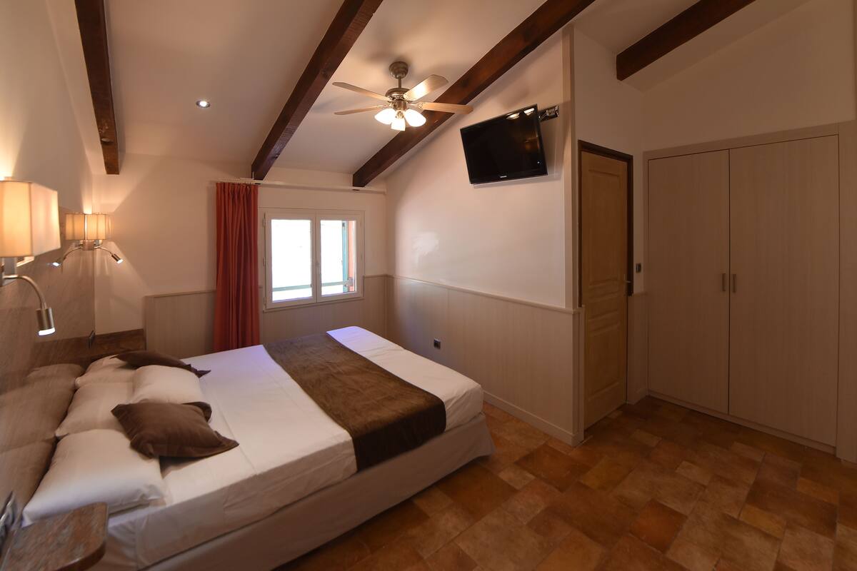 Un dormitorio con cama, ventilador de techo, televisor, armario y ventana con cortinas.