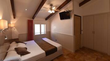 A bedroom with a bed, a ceiling fan, a TV, a wardrobe, and a window with curtains.