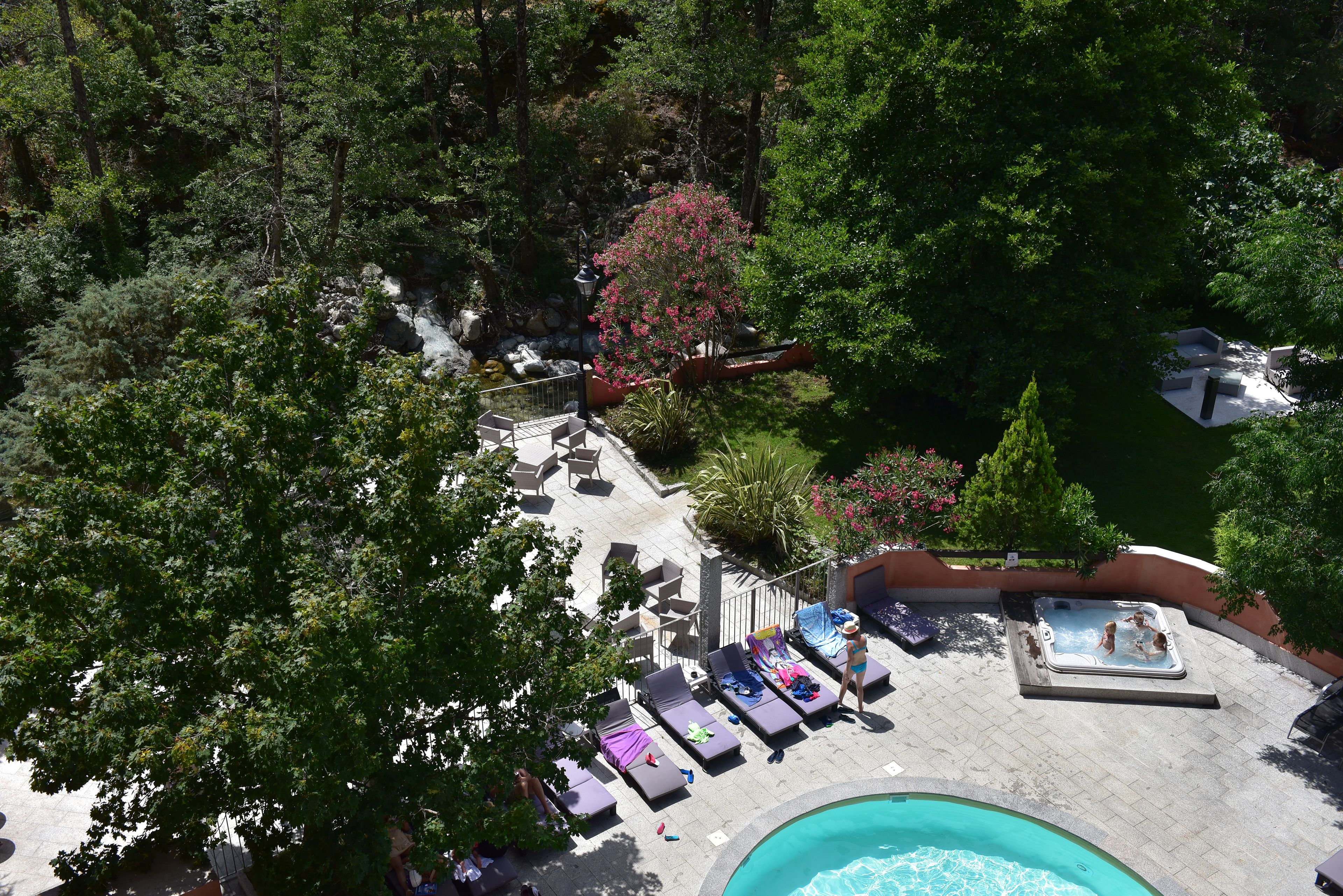 A rooftop pool area with lounge chairs, a hot tub, and a view of the surrounding forest.