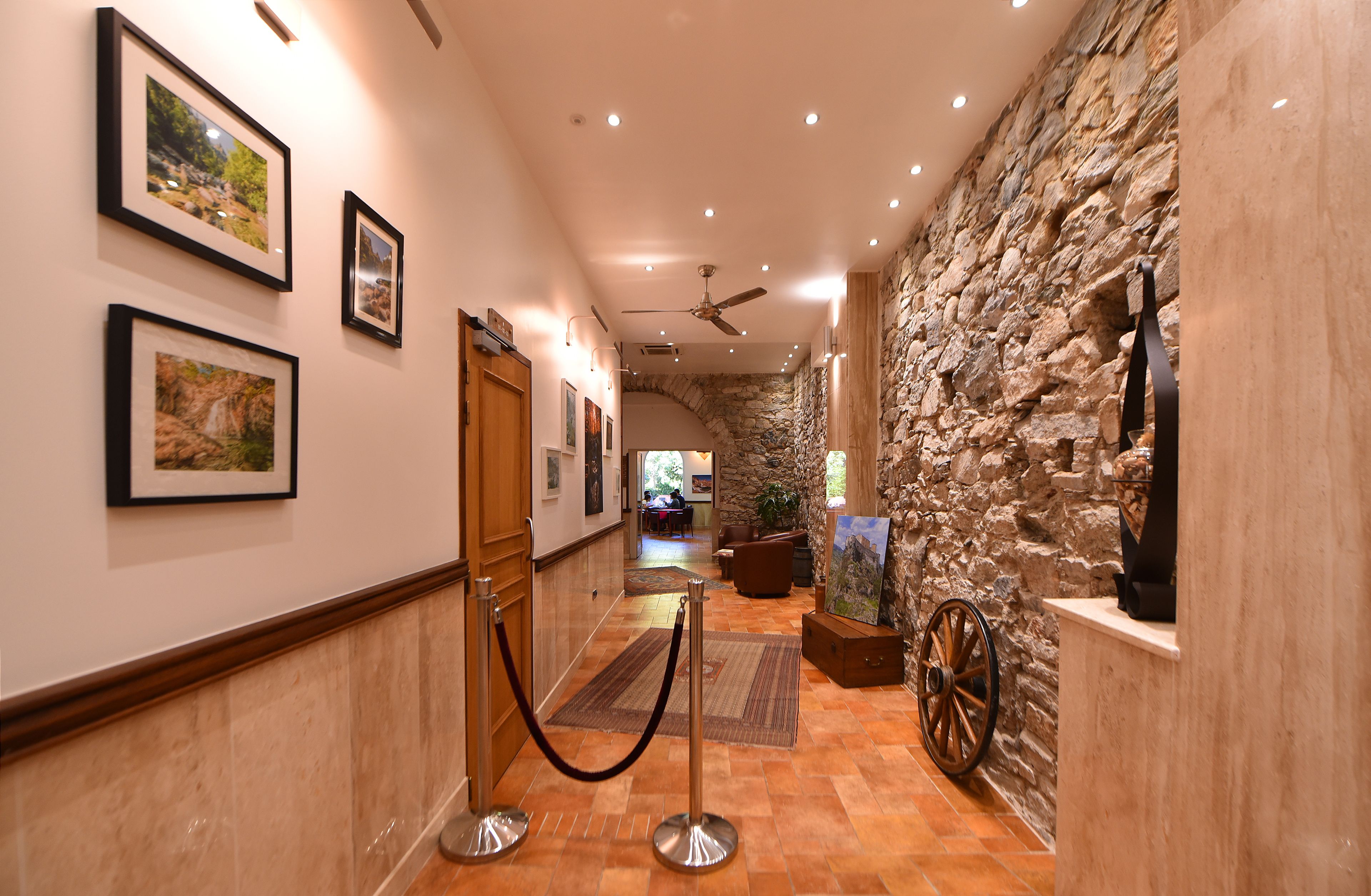 A hallway with framed pictures on the walls, a stone wall on one side, and a wooden door at the end.