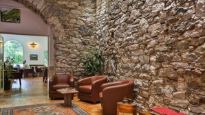 Un vestíbul amb parets de pedra, butaques de cuir, una catifes amb motius i una taula de fusta amb llibres i un tonell.