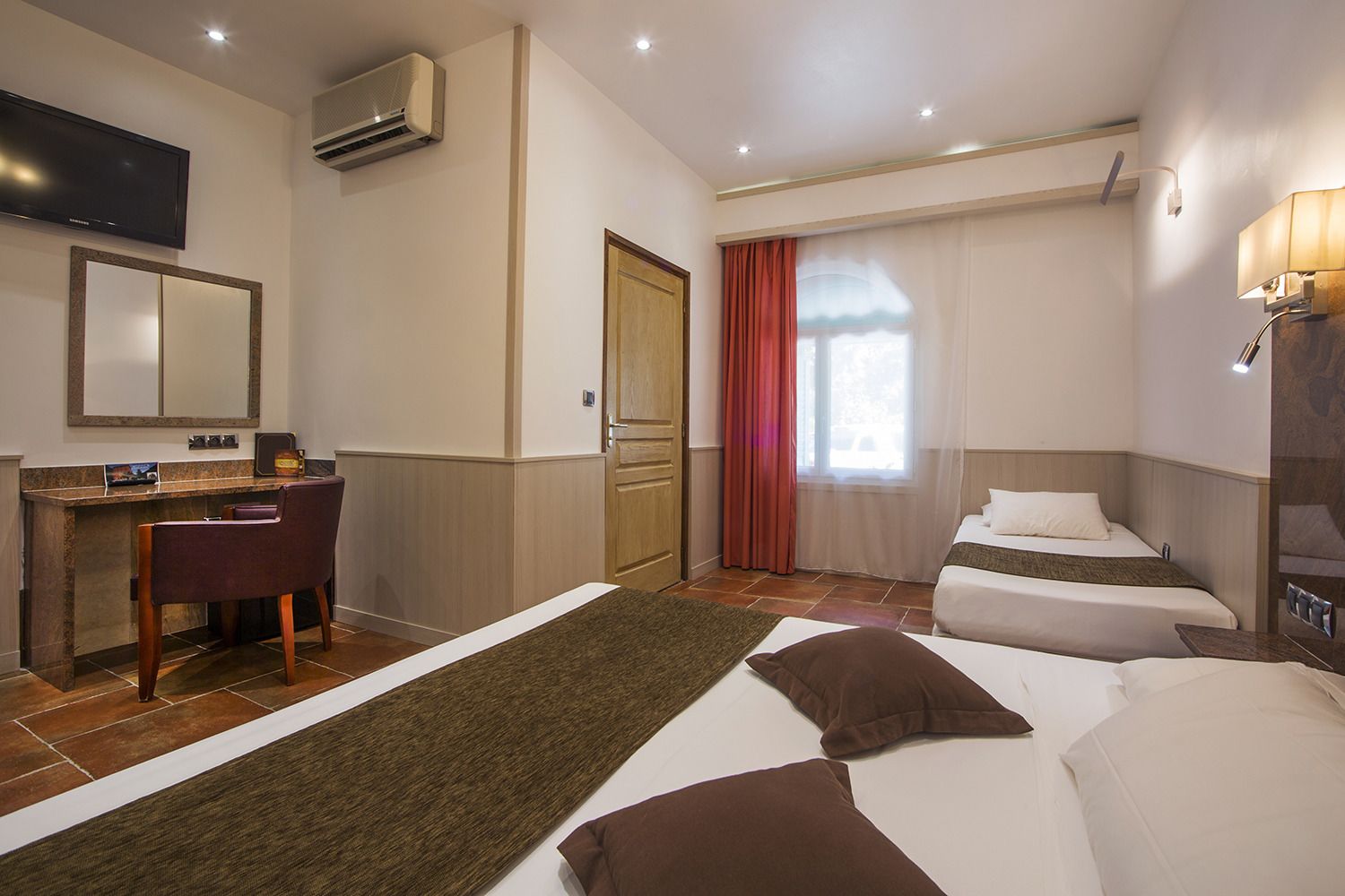 Une chambre d’hôtel équipée d’un bureau, d’une chaise, de deux lits, d’une télévision et d’un appareil de climatisation.