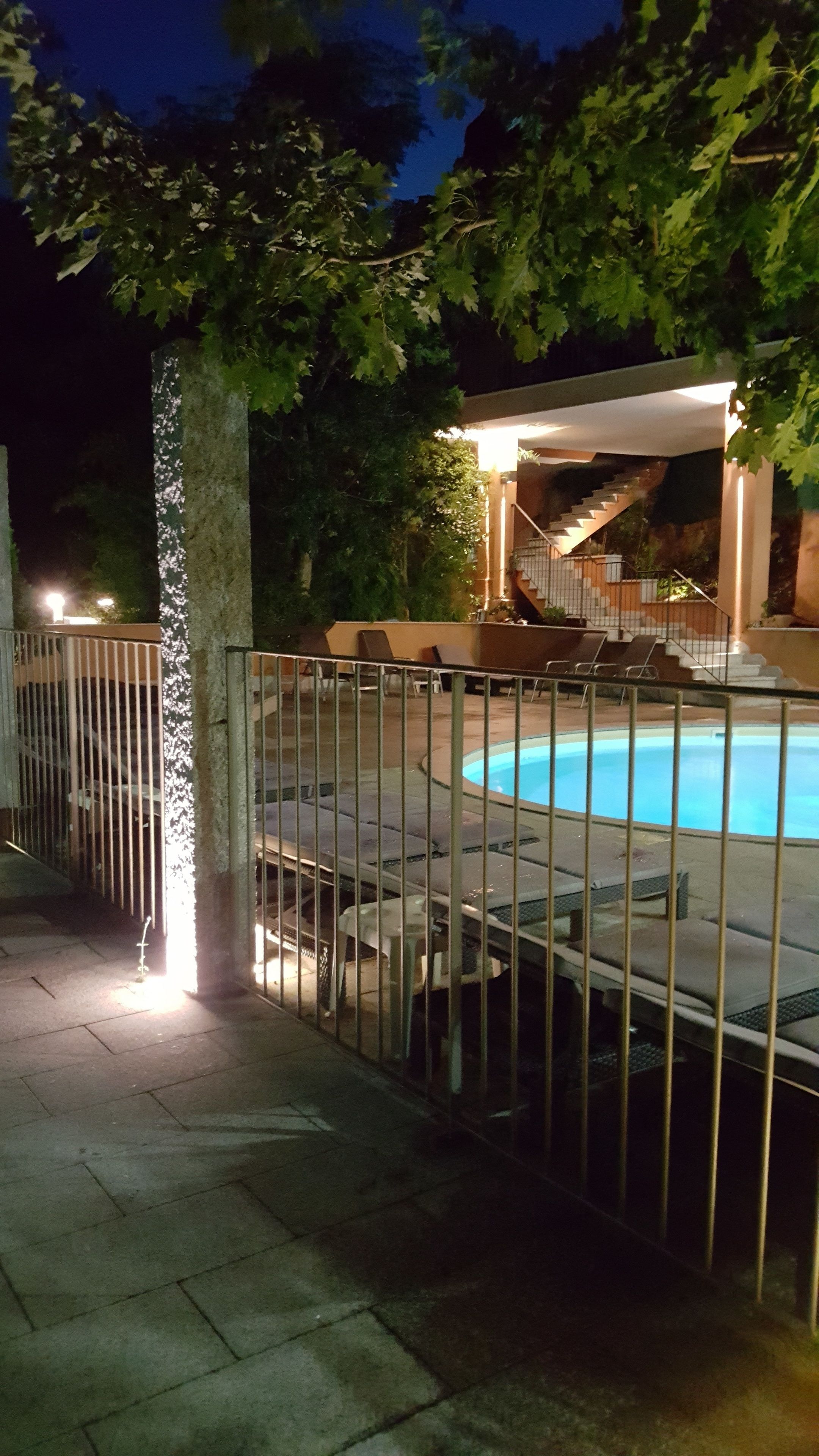 A swimming pool with a metal fence, a covered seating area, and a staircase leading to a building.