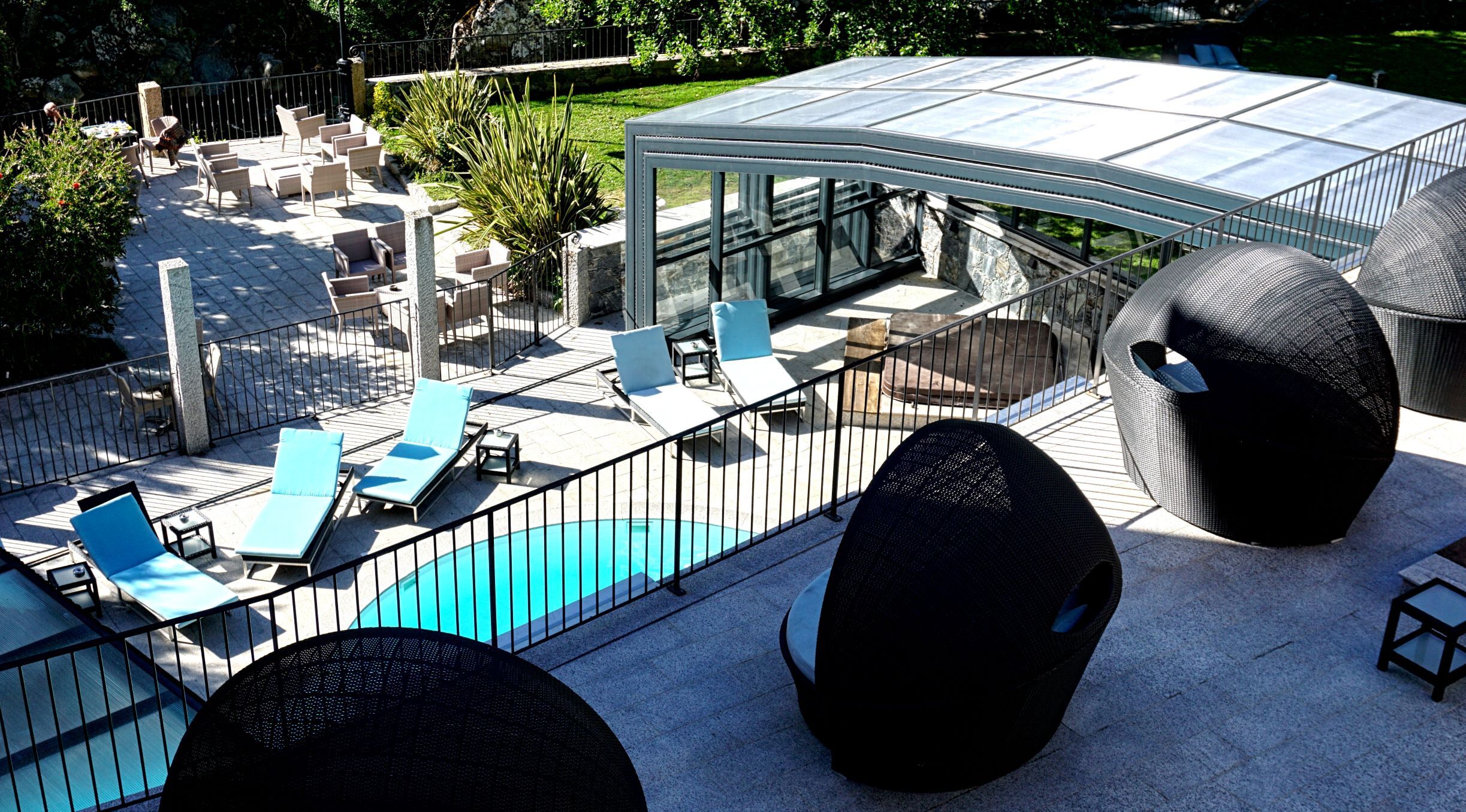 A rooftop pool area with lounge chairs, a glass-enclosed patio, and a view of the surrounding greenery.