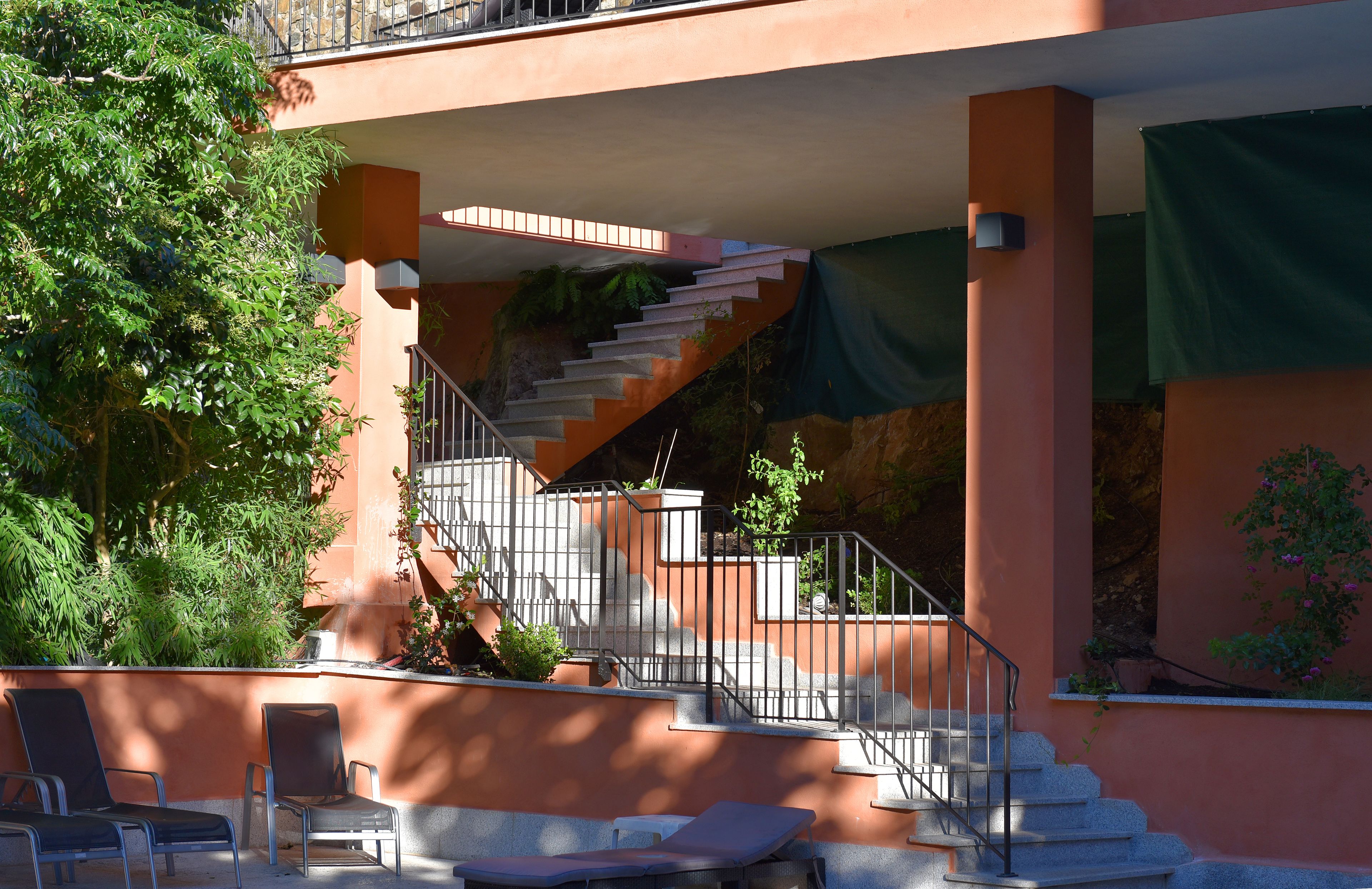 Un edificio con una escalera que lleva a un nivel superior, asientos exteriores con sillas y un árbol.