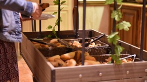 Buffet amb diferents tipus de pa i pastissos en cistos de vimetla, una persona servint menjar, i una taula de fusta en un espai de cuina.