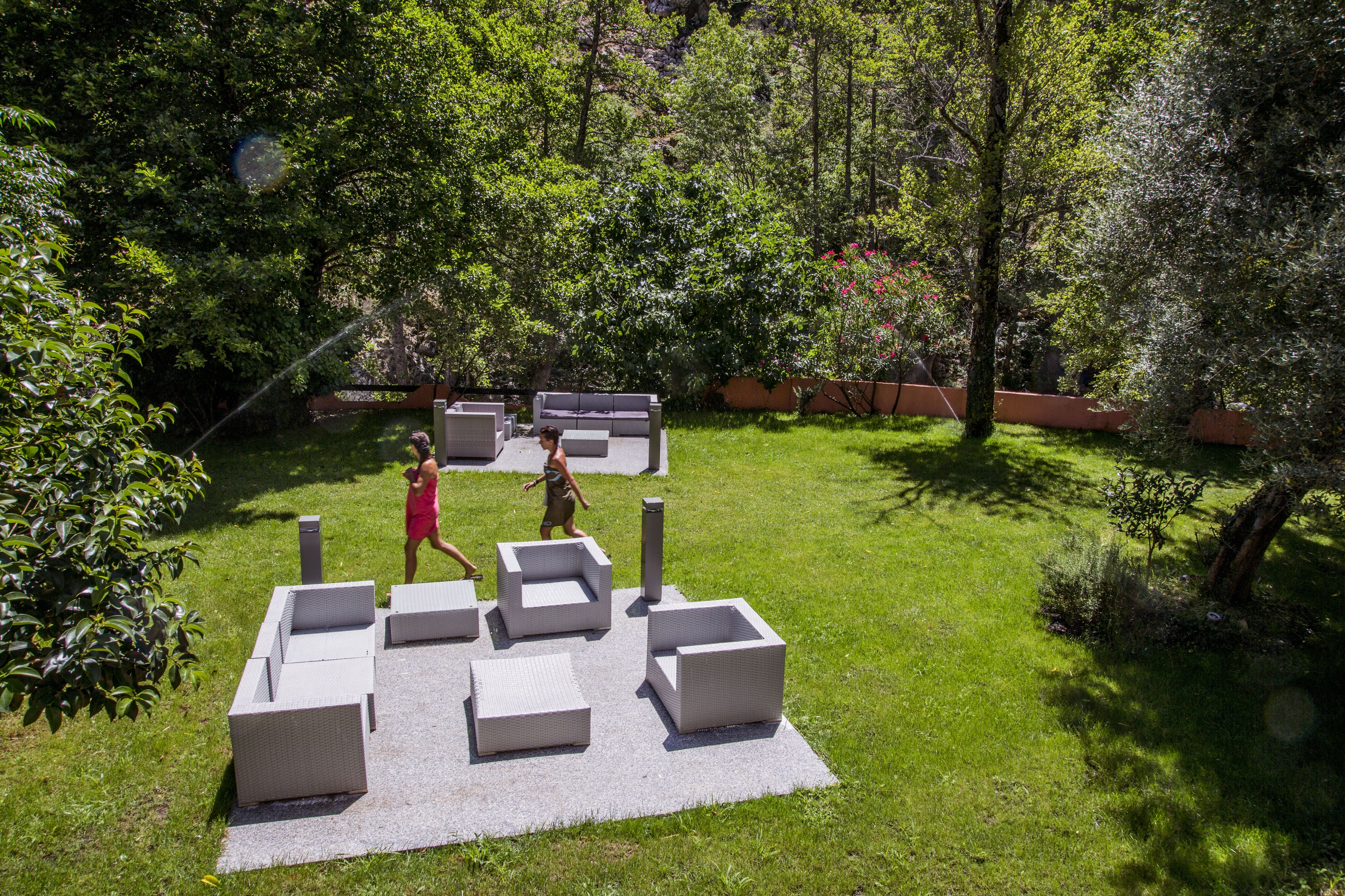 Een terras met modern, geometrisch meubilair, gelegen op een gazon omringd door weelderige beplanting.
