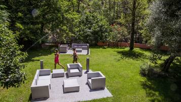Een terras met modern, geometrisch meubilair, gelegen op een gazon omringd door weelderige beplanting.