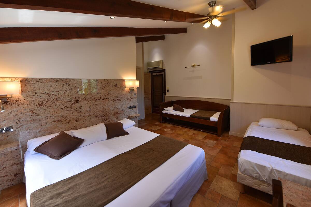 Habitación de hotel con una cama grande, una cama más pequeña, un televisor y una pared decorativa de piedra.