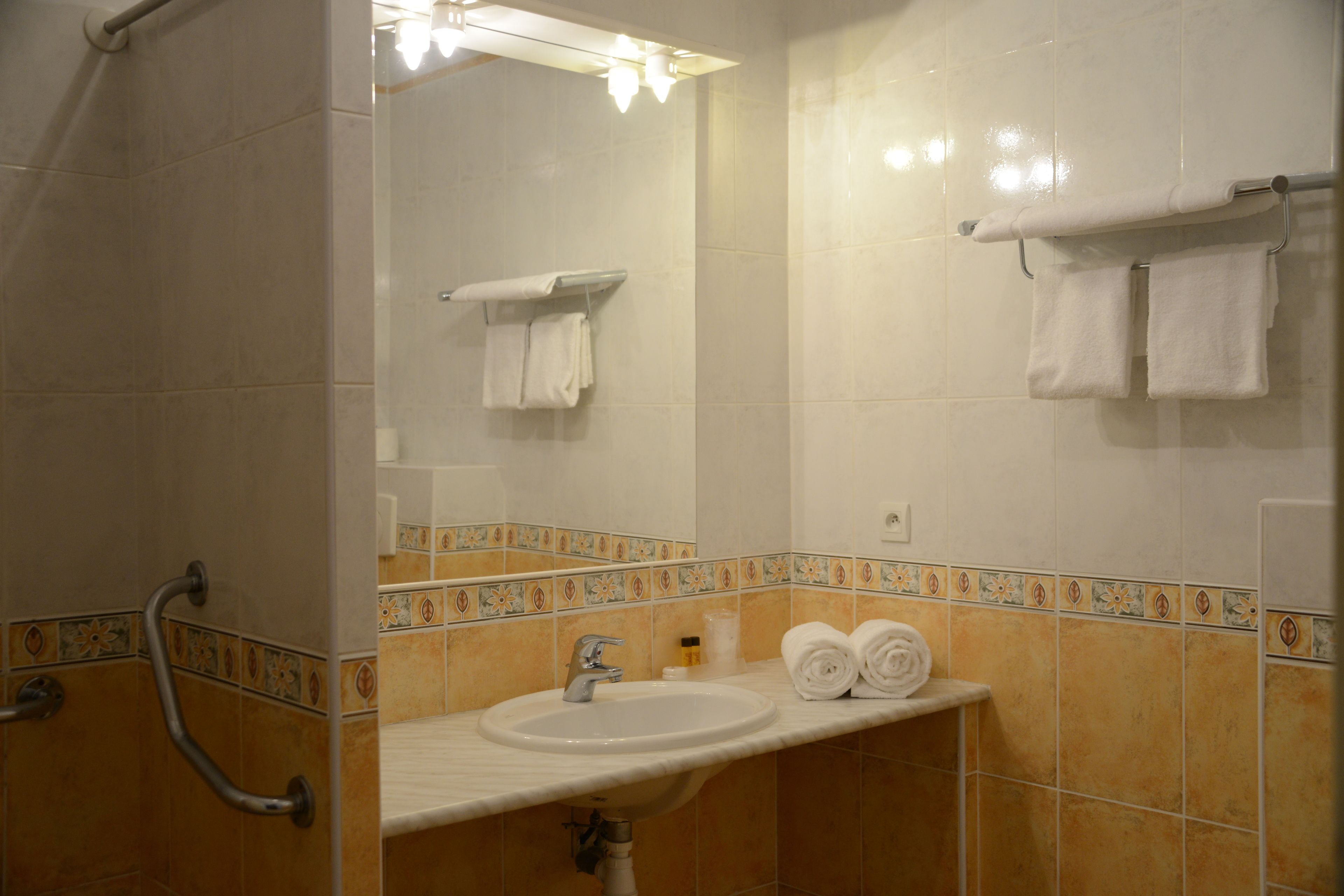 A bathroom with a sink, mirror, and handrails.