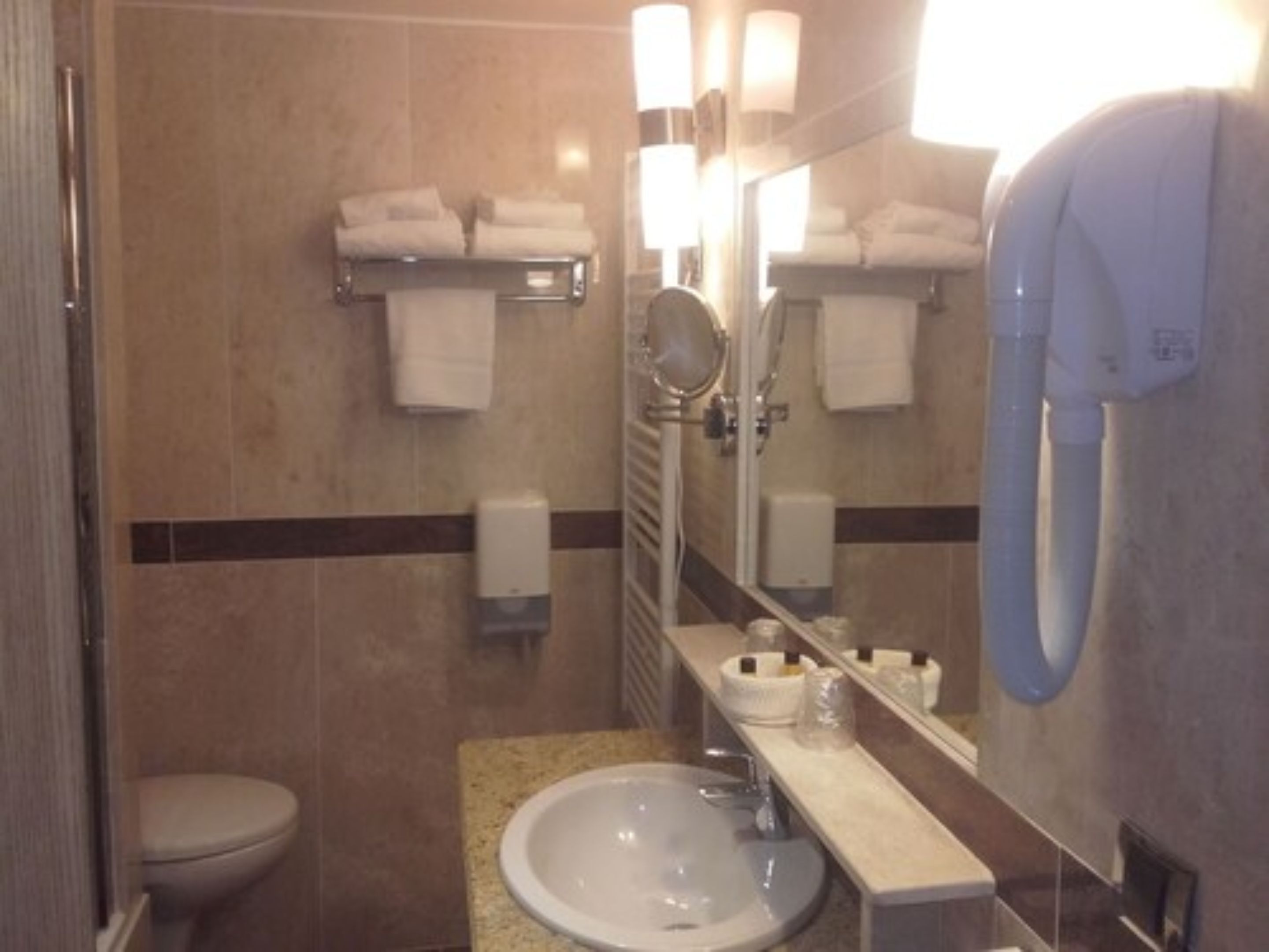 Un bany d'hotel amb vàter, rentapeus, mirall, assecagordes i assecador de mans.