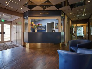 A reception area with a reception desk, a blue seating area, and a vending machine. - Hotel Zwanenburg (Zwanenburg)