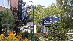 A hotel sign with the name "Hotel Zwanenburg" in a garden setting with various plants and a building in the background. - Hotel Zwanenburg (Zwanenburg)