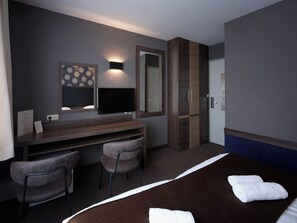 A hotel room with a bed, a desk with two chairs, a flat-screen TV, a large mirror, and a door. - Hotel Zwanenburg (Zwanenburg)
