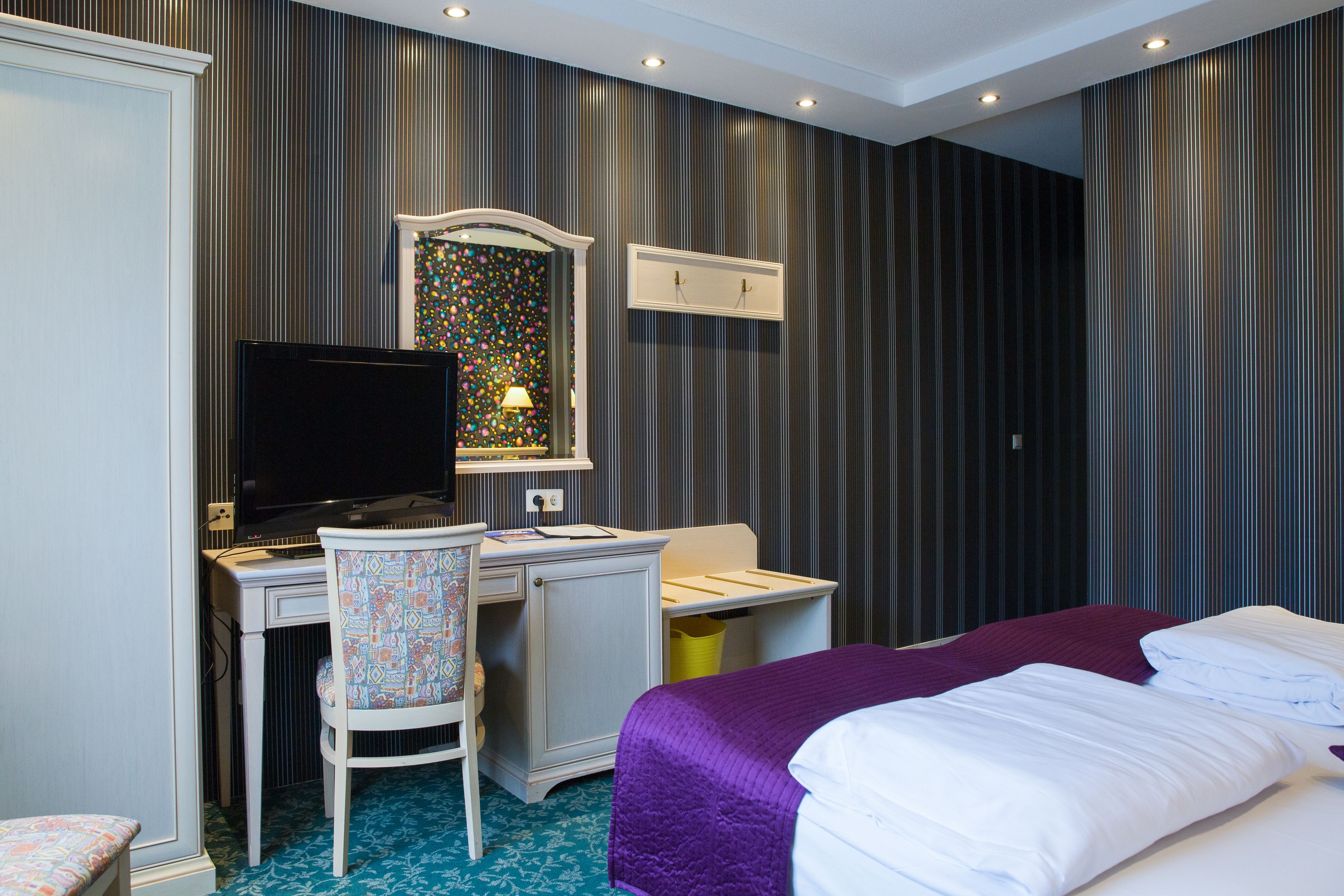 A hotel room with a bed, a desk with a computer, a chair, and a window with curtains.