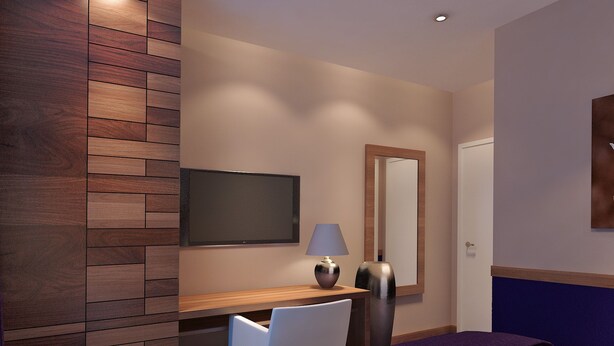 A hotel room with a bed, a desk, a chair, a TV, a lamp, and a mirror. - Hotel Zwanenburg (Zwanenburg)
