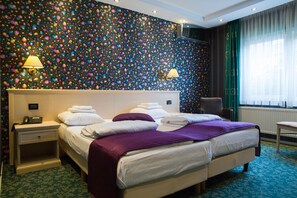 A hotel room with a large bed, two bedside tables, a chair, and a patterned wall. - Hotel Zwanenburg (Zwanenburg)