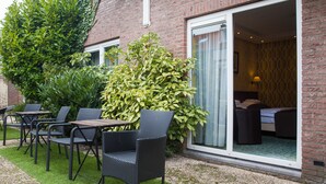 A hotel room with a bed, a window with curtains, and a small balcony with a chair and table. - Hotel Zwanenburg (Zwanenburg)