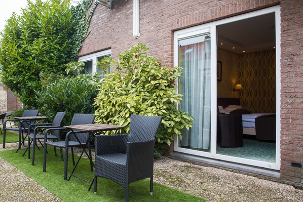 A hotel room with a bed, a window with curtains, and a small balcony with a chair and table. - Hotel Zwanenburg (Zwanenburg)