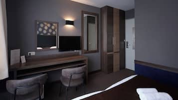A hotel room with a bed, a desk with two chairs, a flat-screen TV, a large mirror, and a door.