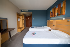 A hotel room with two beds, a desk, and a TV. There is a hallway leading to another room. - Idea Hotel Torino Mirafiori (Turin)