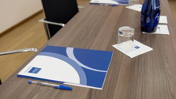 A conference table with a blue and white folder, a pen, a glass, and a water bottle.