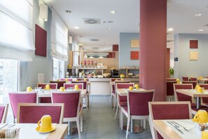 A modern dining area with red upholstered chairs, yellow tableware, and a central counter with kitchen appliances. - Idea Hotel Torino Mirafiori (Turin)
