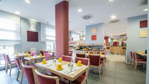 A modern restaurant with multiple dining tables and chairs, a central pillar, and a view of the kitchen area. - Idea Hotel Torino Mirafiori (Turin)