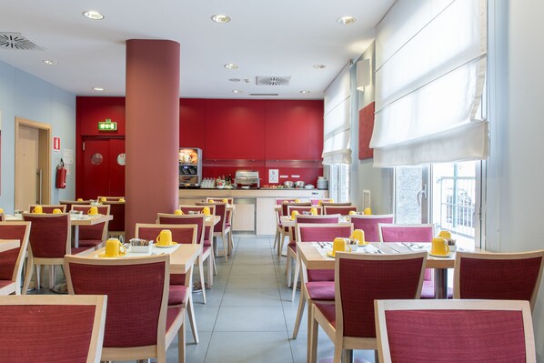 A modern restaurant with red and white decor, multiple dining tables, and a central kitchen area. - Idea Hotel Torino Mirafiori (Turin)