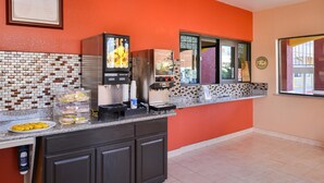 A kitchen area with a coffee machine, a juice dispenser, and a counter with food items. - Americas Best Value Inn Baytown (Baytown)