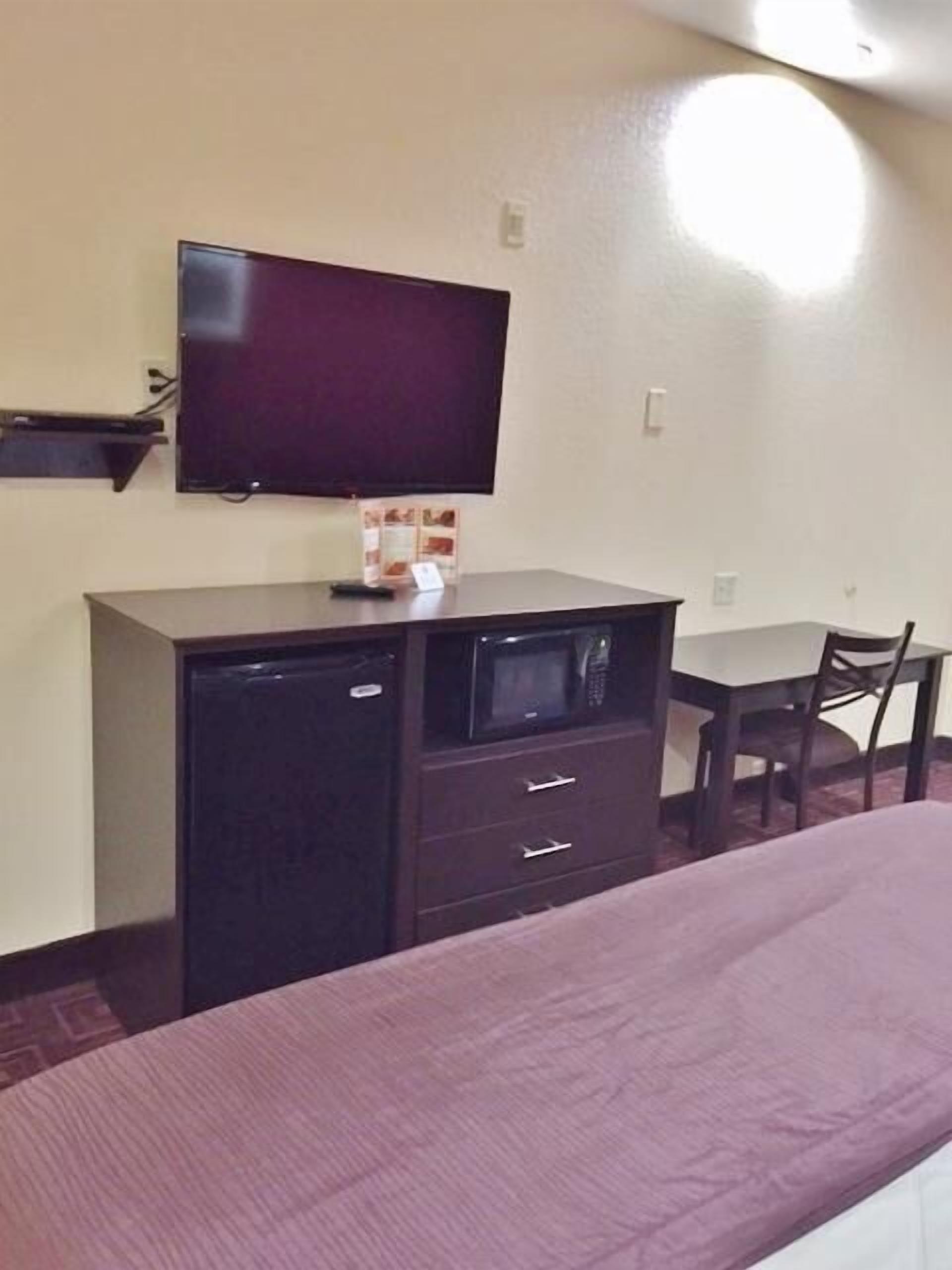 A room with a bed, a desk, a chair, a television mounted on the wall, and a small cabinet.