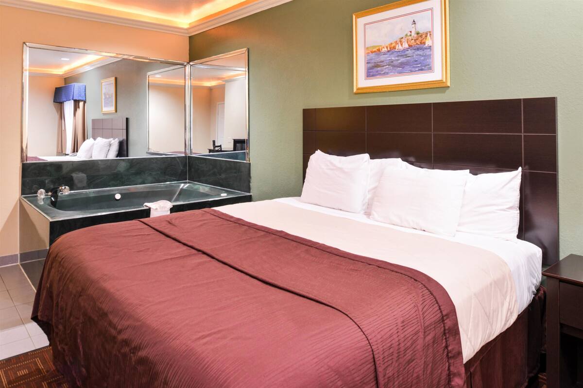 A hotel room with a large bed, a bathroom with a bathtub, and a large mirror.