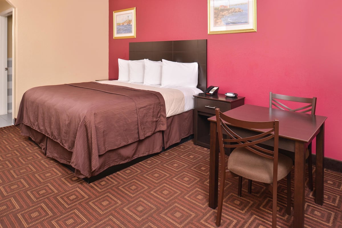 A hotel room with a bed, a bedside table with a phone, a chair, and a table.