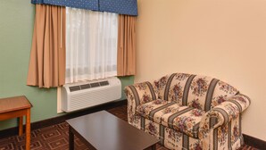 A room with a patterned sofa, a small wooden table, and a radiator. - Americas Best Value Inn Baytown (Baytown)