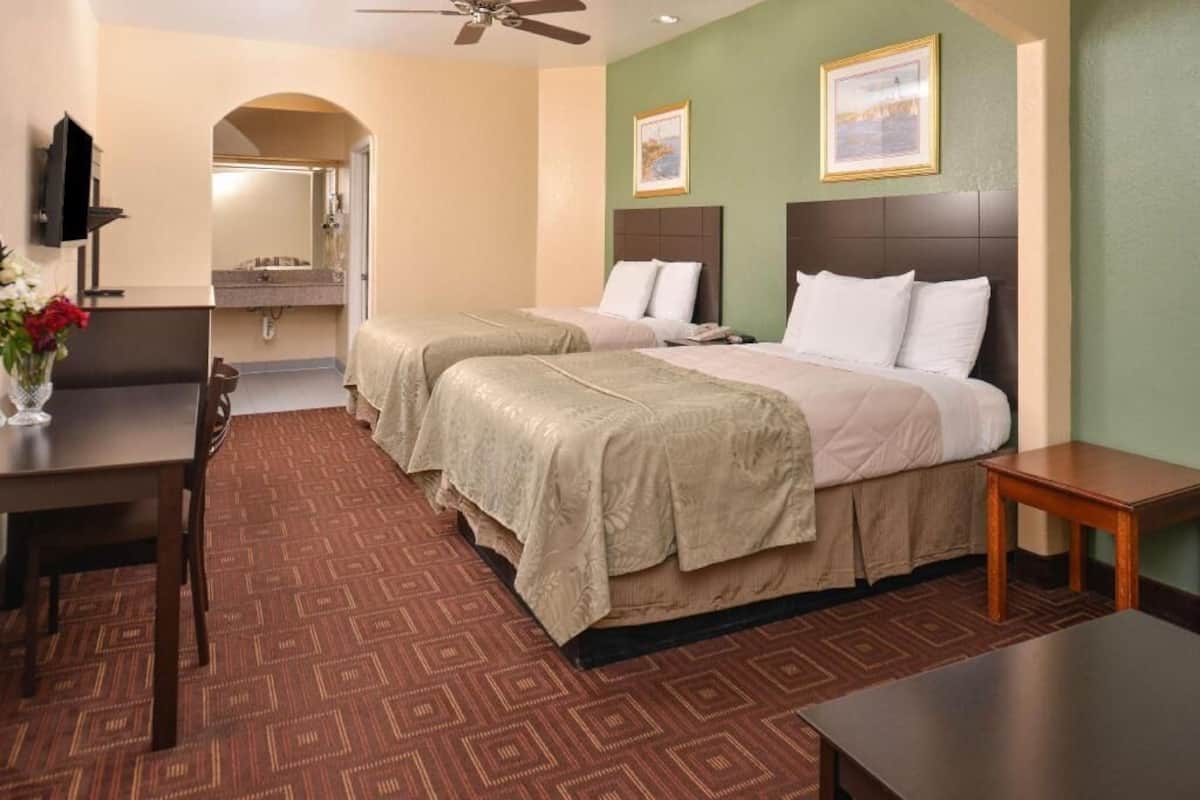 A hotel room with two beds, a desk, a chair, a TV, and a bathroom visible through an archway.