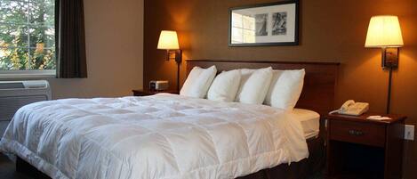 A hotel room with a large bed, two bedside lamps, a nightstand with a phone, and a window with curtains.