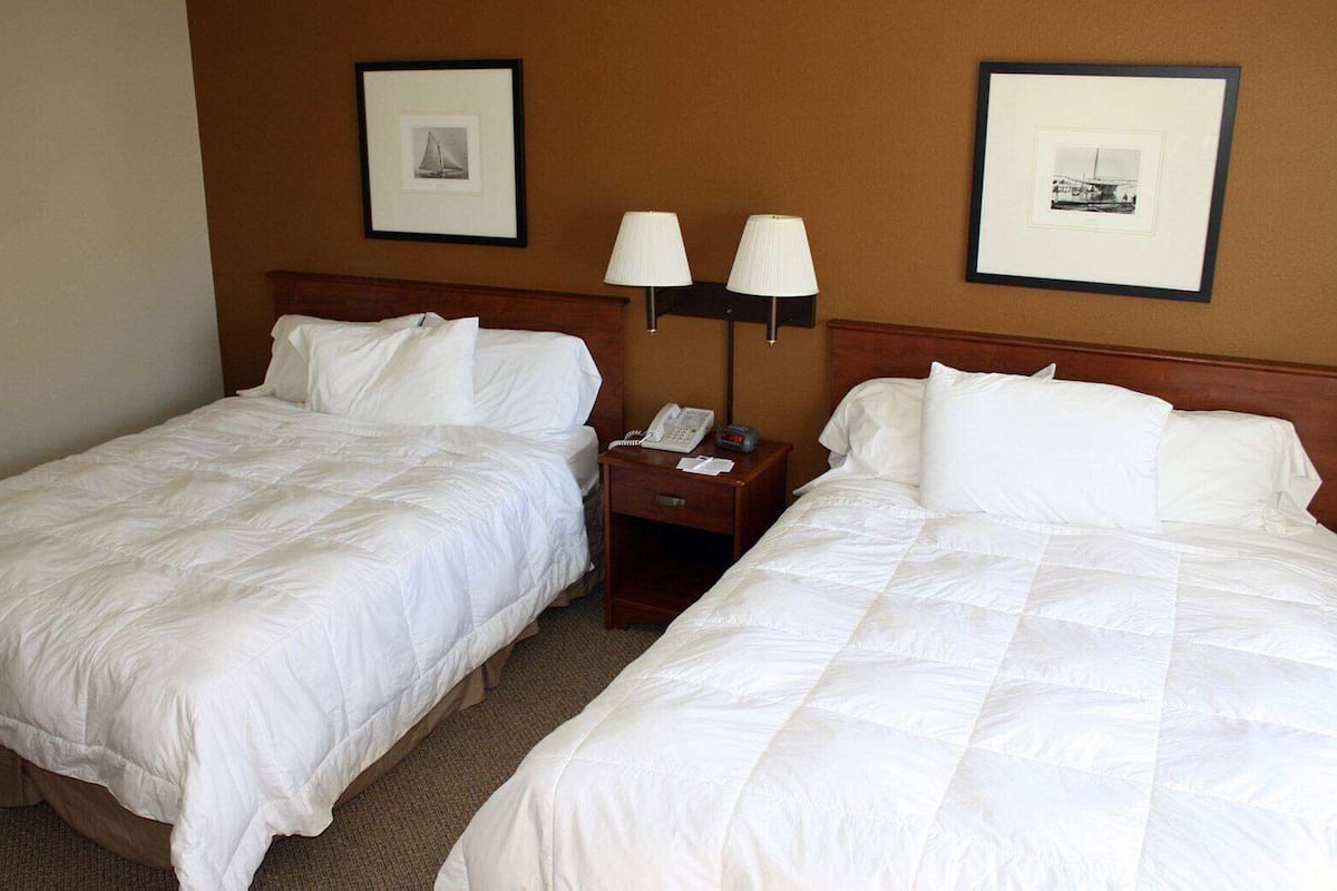 A hotel room with two beds, a nightstand with a lamp, and framed pictures on the wall.